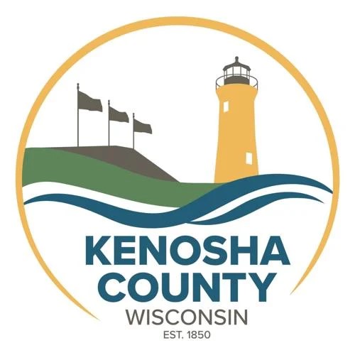 Kenosha County Logo, circle with yellow lighthouse and three gray flags over a green and blue wavy line